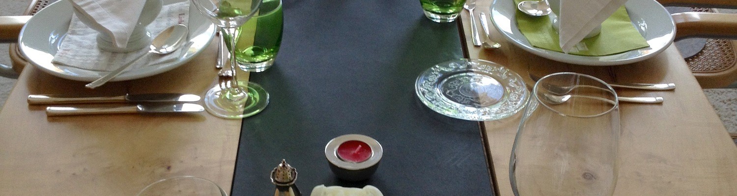 Ein gedeckter Tisch mit grünen Gläsern und Silberbesteck