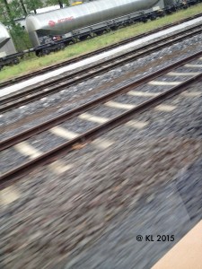 Ein Zug fährt und aus dem Fenster geht der Blick auf die Gleise